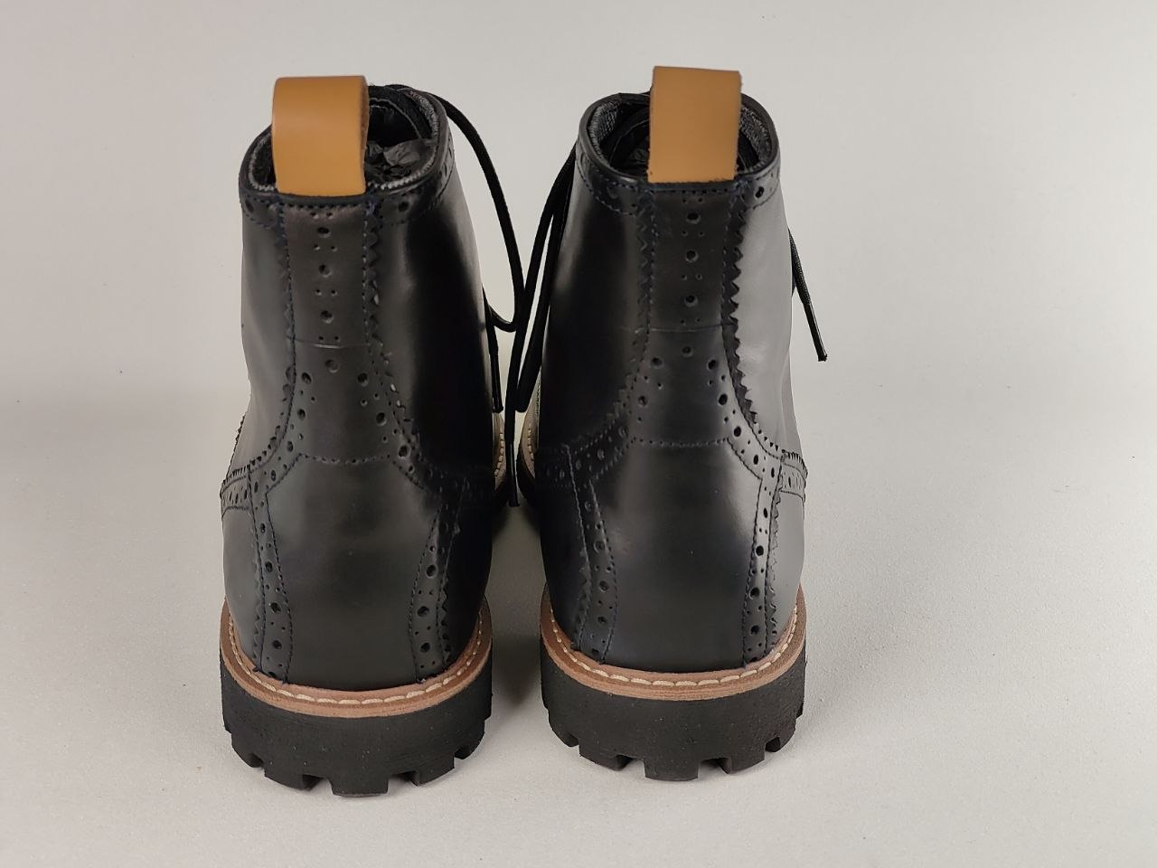 Pair of black leather boots with brown soles on a light gray background