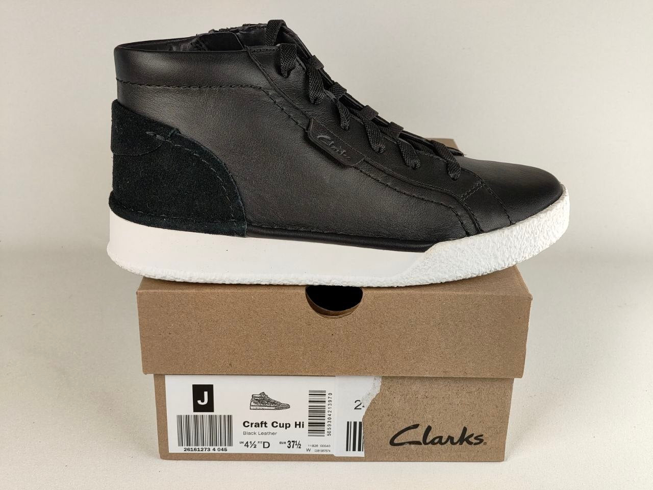 Black high-top sneaker on a Clarks shoe box with a beige background