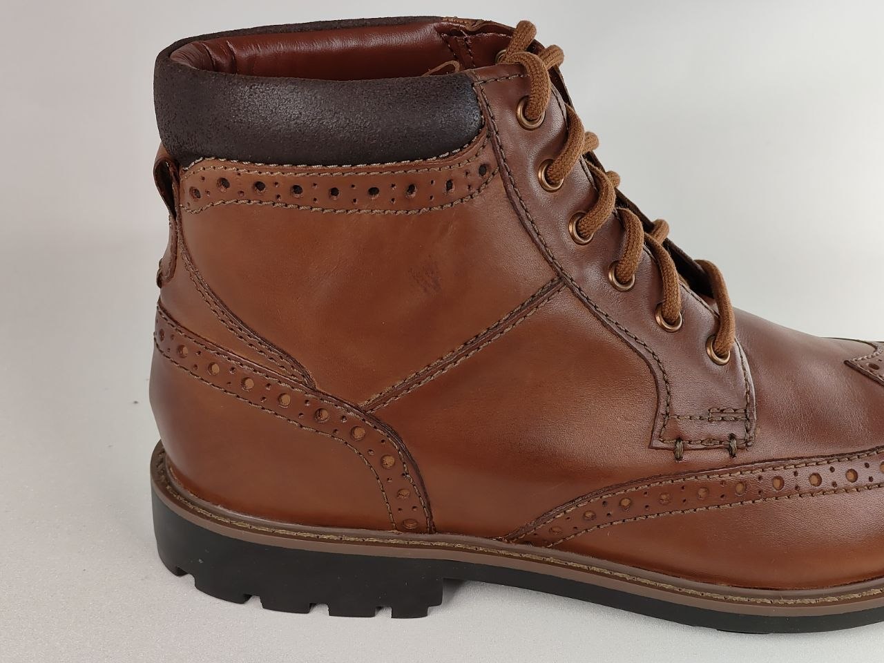 Brown leather boot with black sole on a light gray background