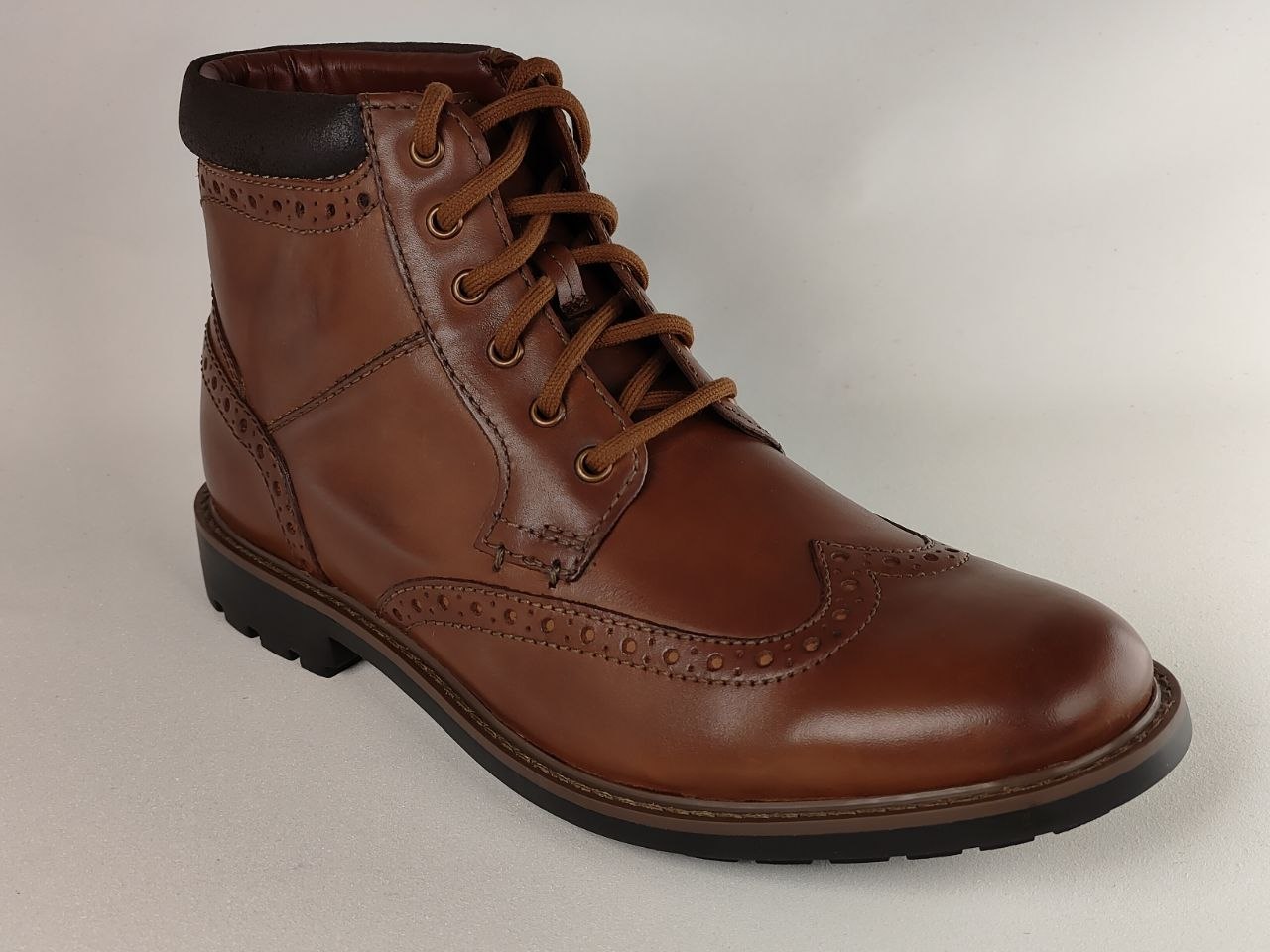 Brown leather boot with black sole on a light gray background
