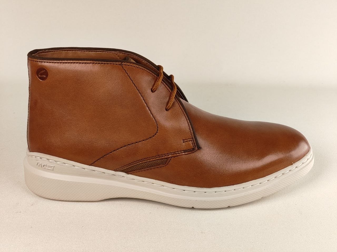 Brown leather boot with white sole on a beige background