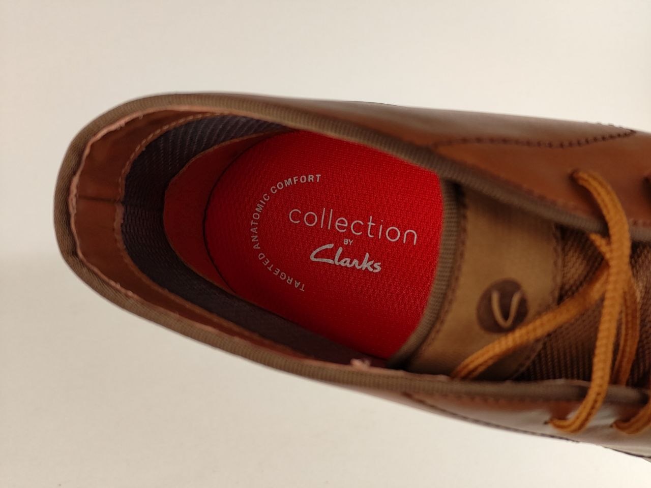 Brown shoe with orange laces and red interior displaying 'Collection by Clarks' on a beige background