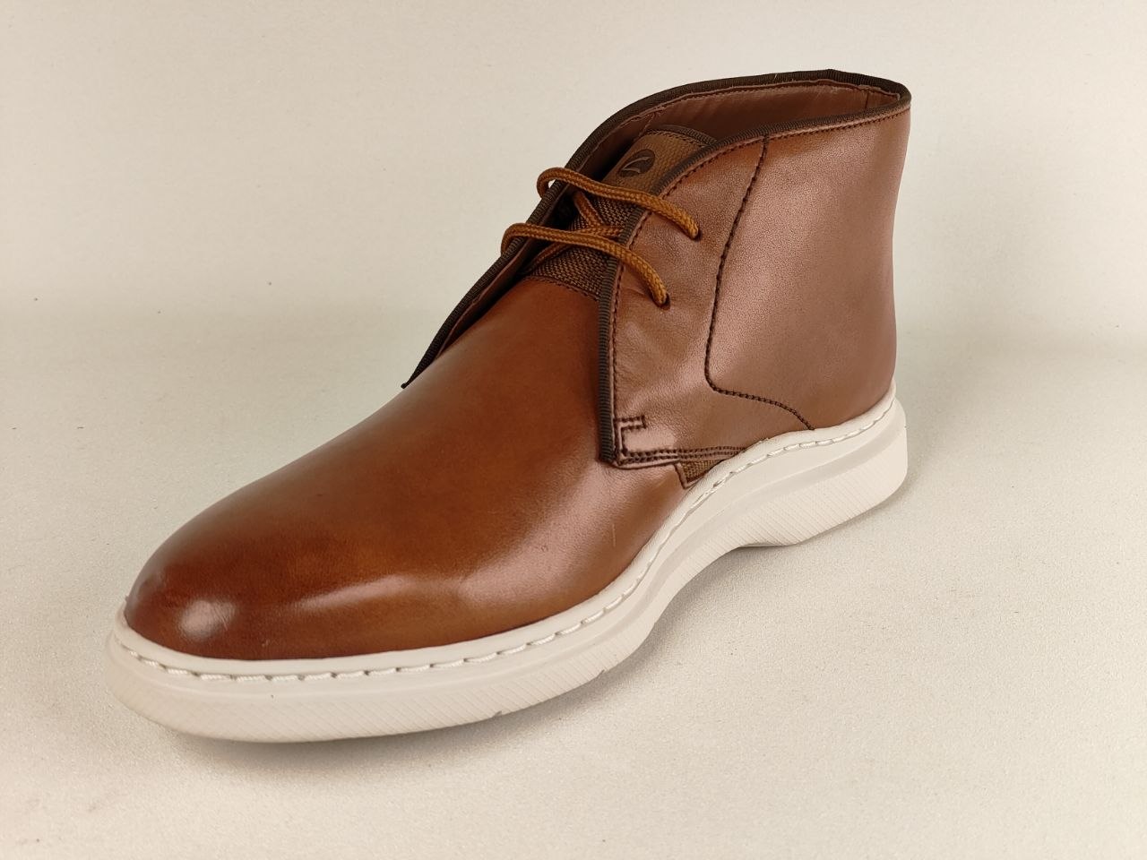 Brown leather boot with white sole on a beige background