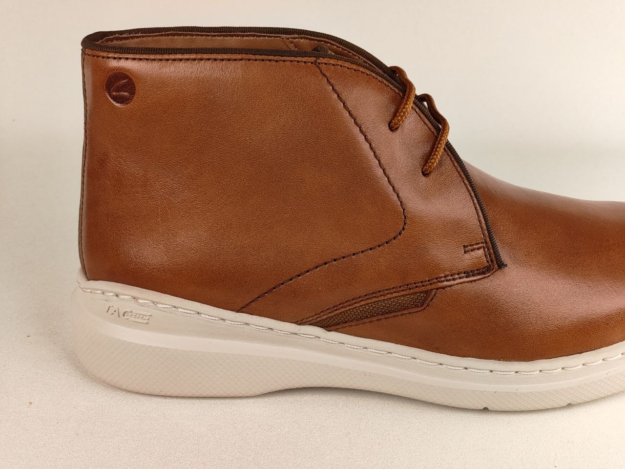 Brown leather boot with a white sole on a beige background