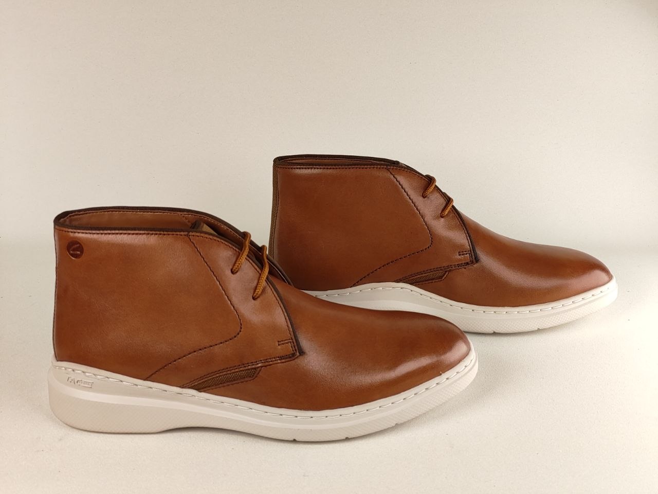 Pair of brown leather boots with white soles on a beige background