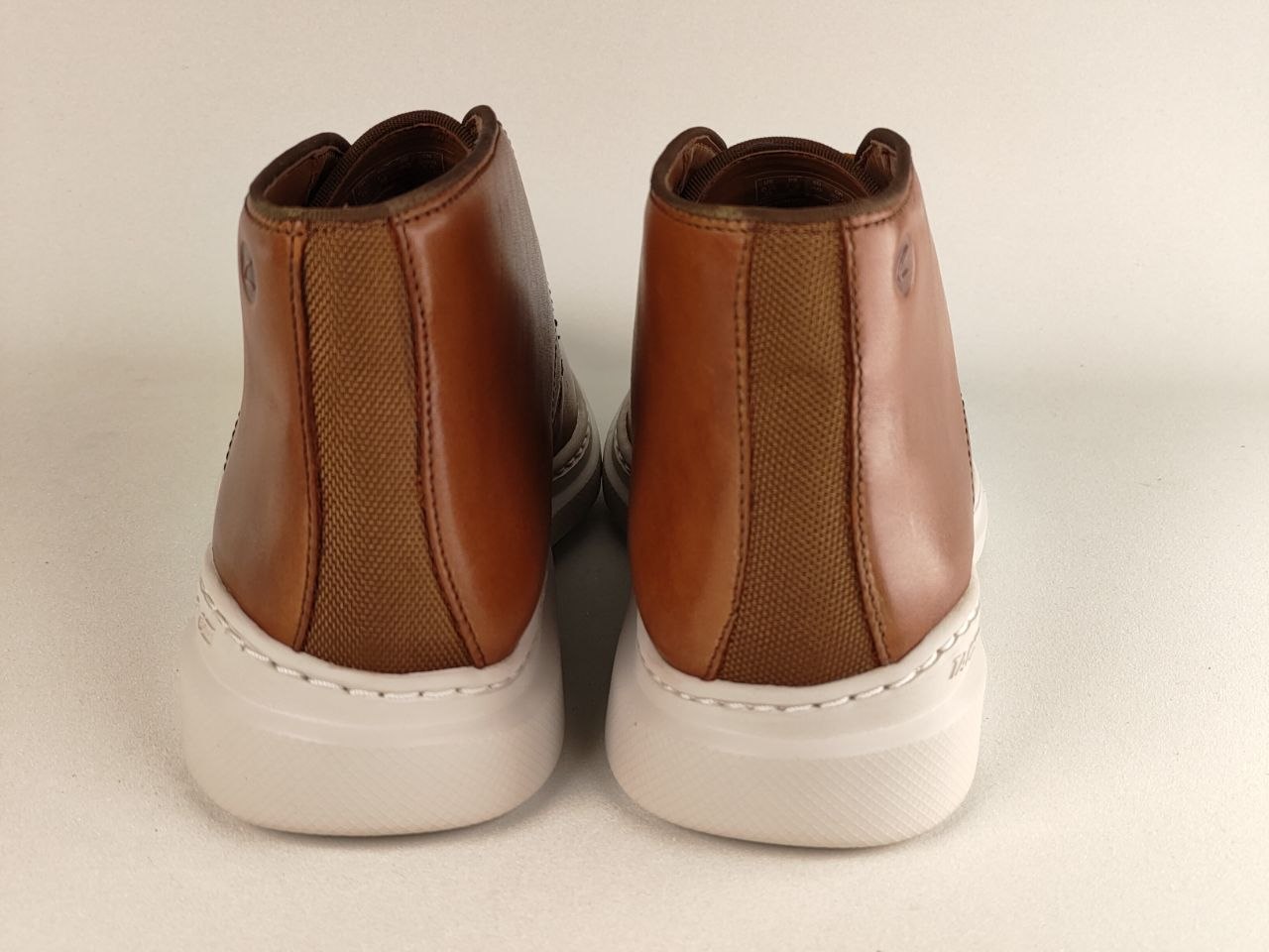 Pair of brown leather boots with white soles on a beige background