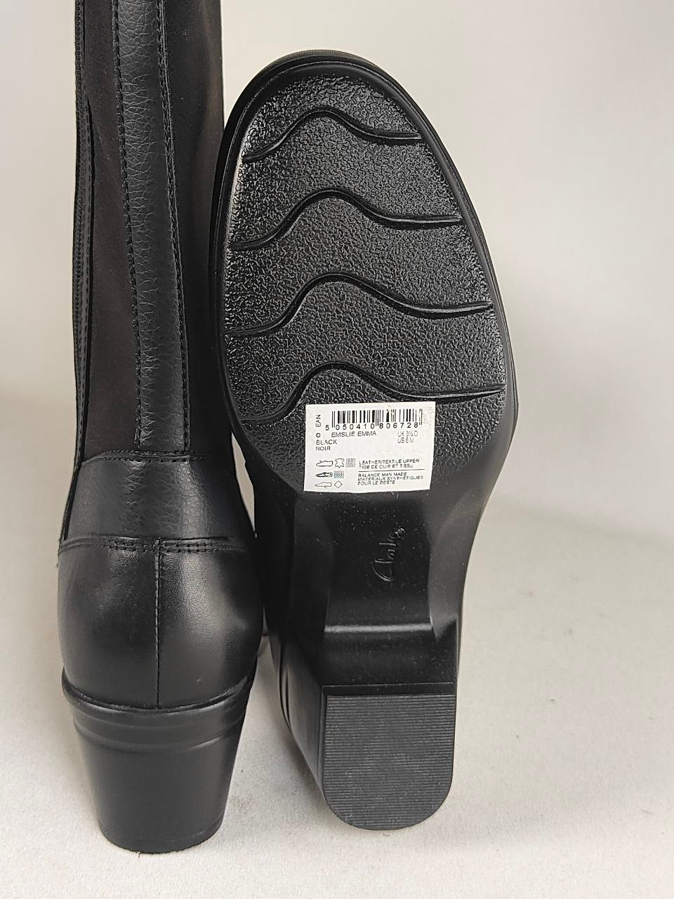 A pair of black leather boots shown from the back, with one boot displaying the heel and sole and the other standing upright to show the shaft.
