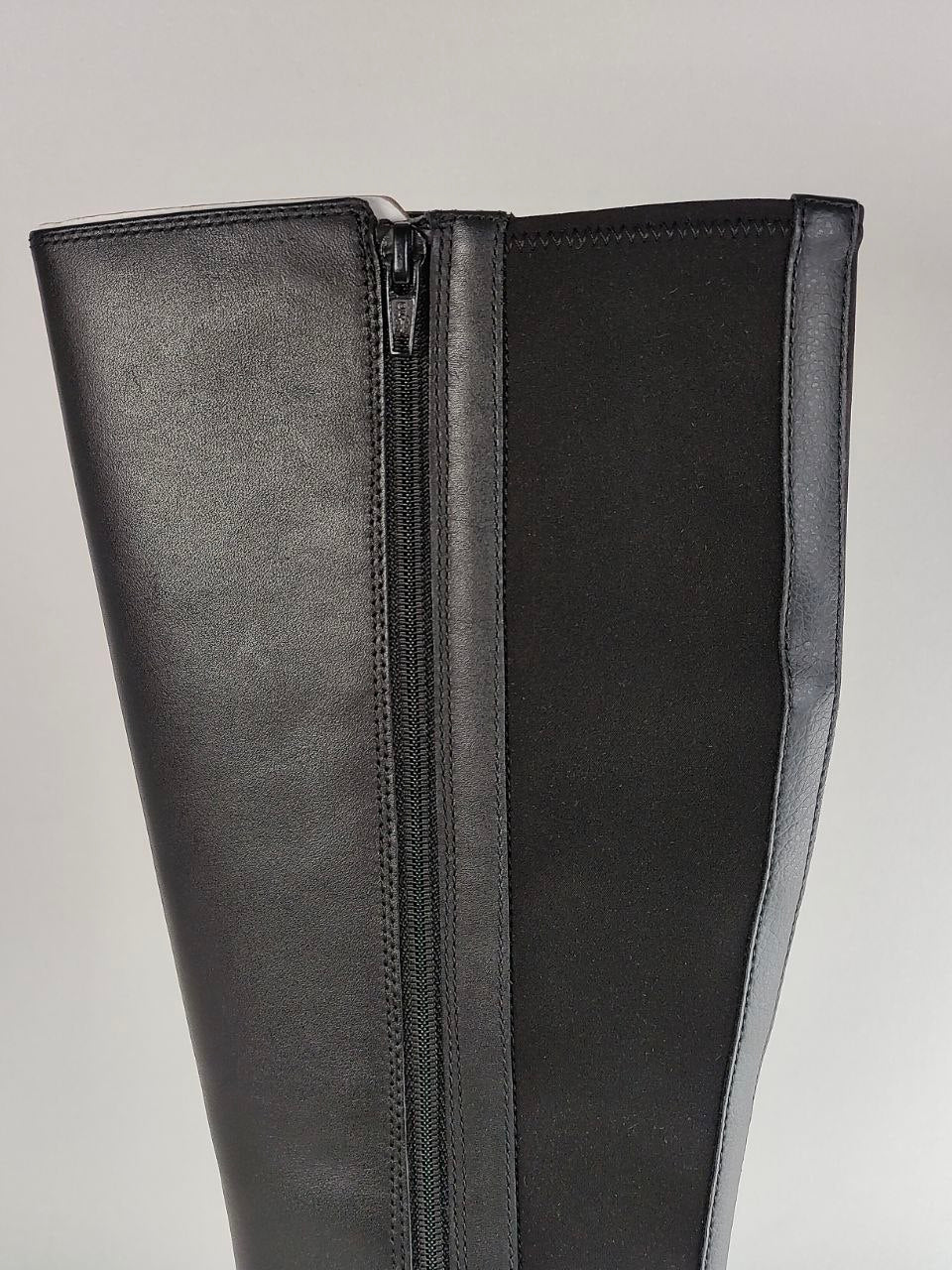 Close-up of a black leather boot with a side zipper, showing the texture of the leather and the zipper detail against a neutral gray background.