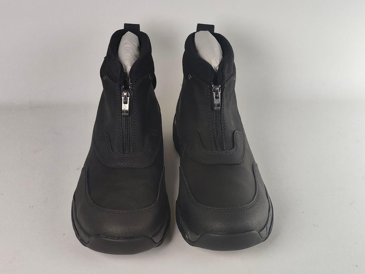 A pair of black ankle boots with front zippers, shown from the front against a light gray background.