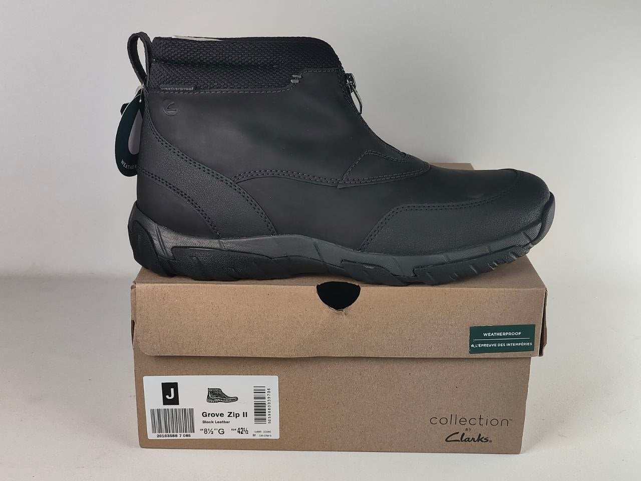 A black Clarks ankle boot shown from the side, resting on top of its brown cardboard shoebox against a light gray background.