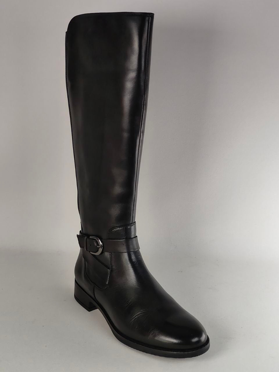 A single black leather knee-high boot with a low block heel and a decorative strap with a buckle detail around the ankle, shown against a plain light gray background.