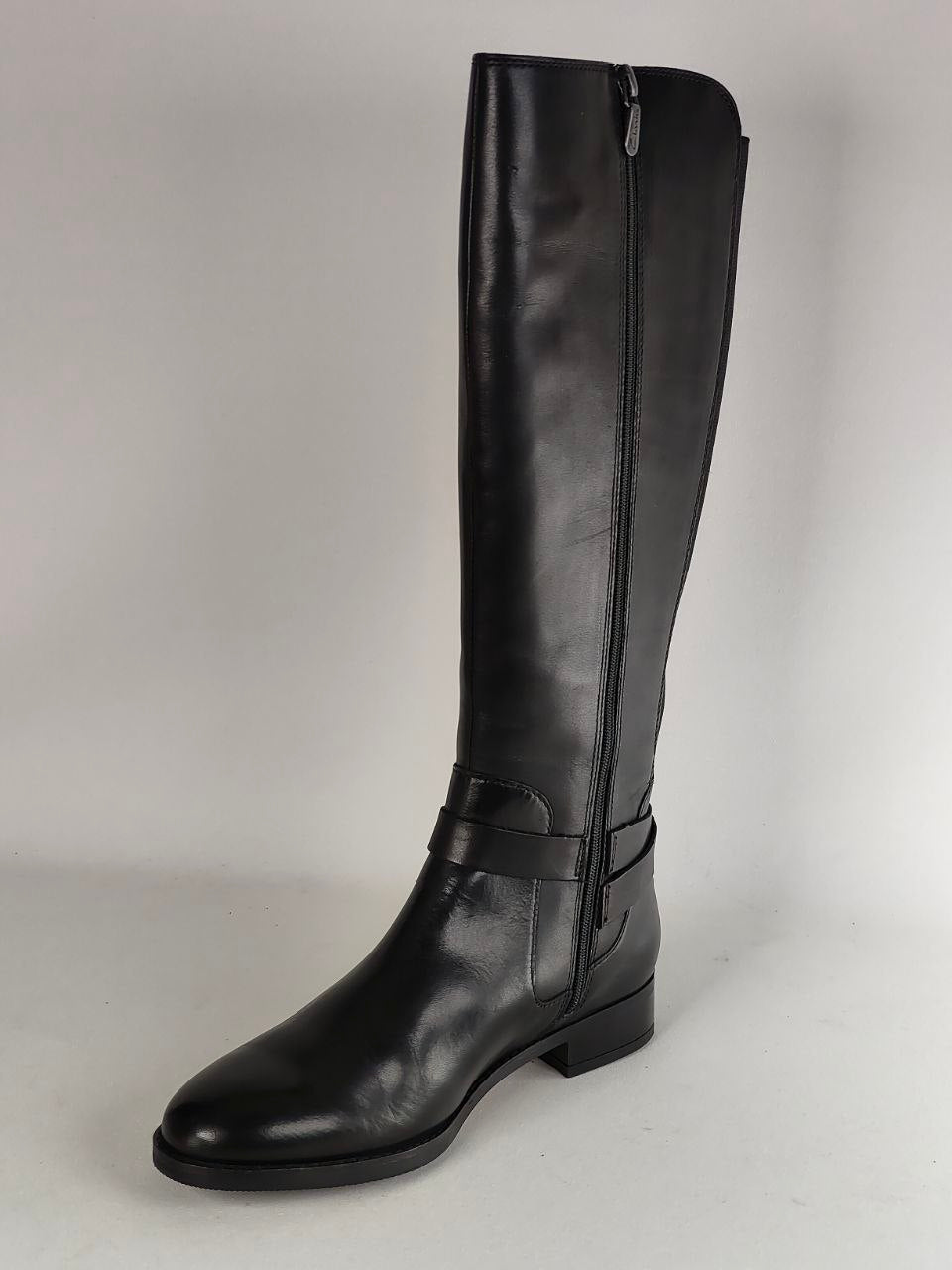 A single black leather knee-high boot with a side zipper and a decorative strap detail around the ankle, shown against a neutral light gray background.