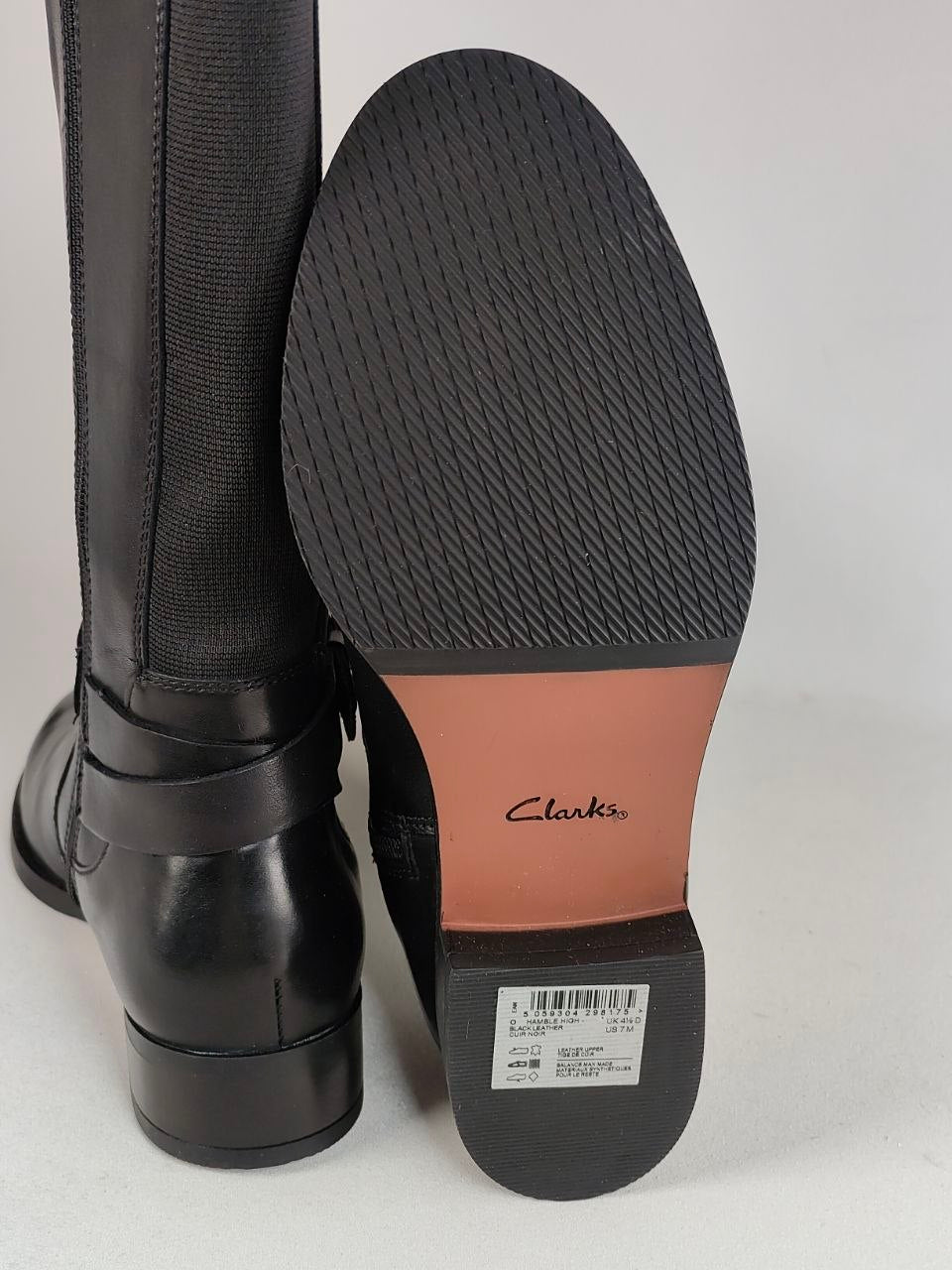 Black leather and textile riding boots shown with one boot standing upright and the other turned to display the sole. The sole has a tan Clarks logo patch and a white size label.