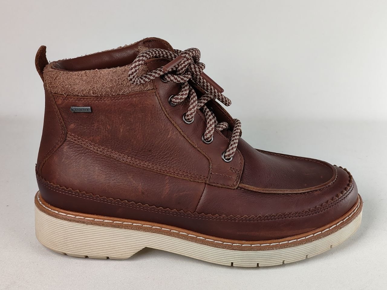 A dark brown leather ankle boot with a thick cream-colored sole and braided brown laces, shown from a side profile view against a light gray background.