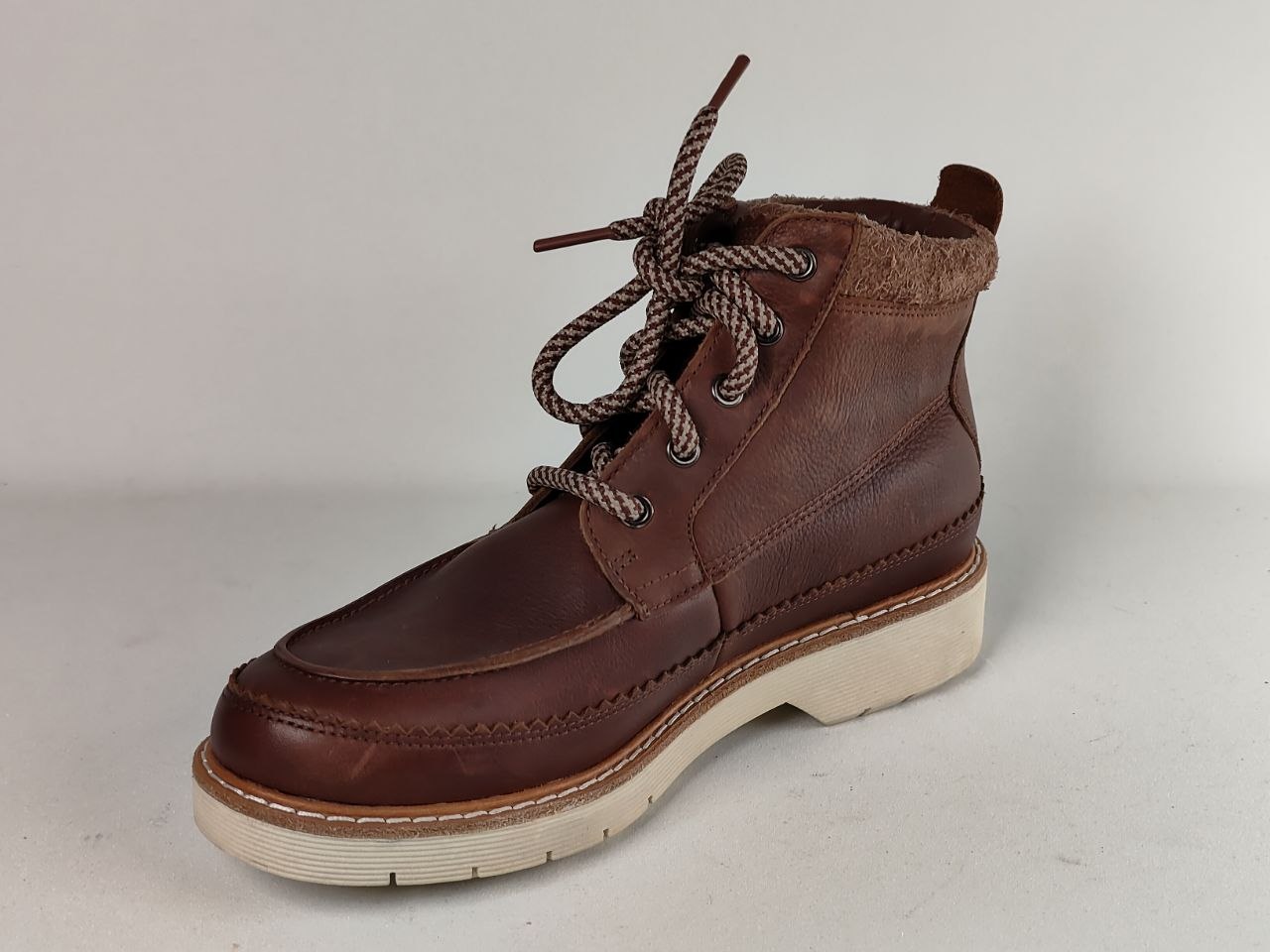 A single brown leather lace-up ankle boot with a thick off-white sole, photographed against a neutral light gray background.