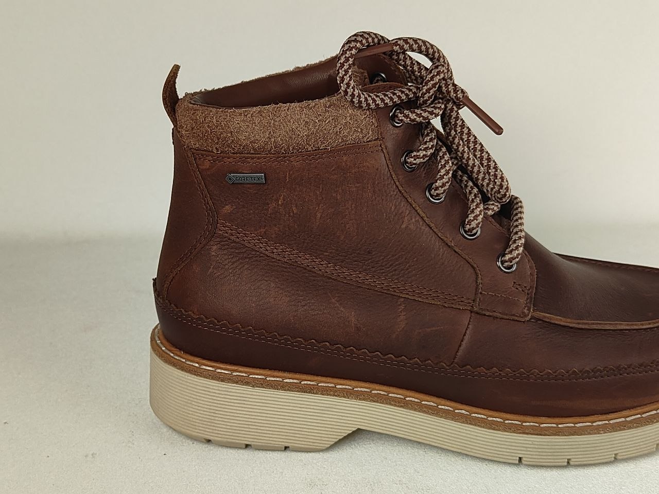 A brown leather lace-up ankle boot with a thick beige sole and brown braided laces, shown from a side profile view against a neutral light background.