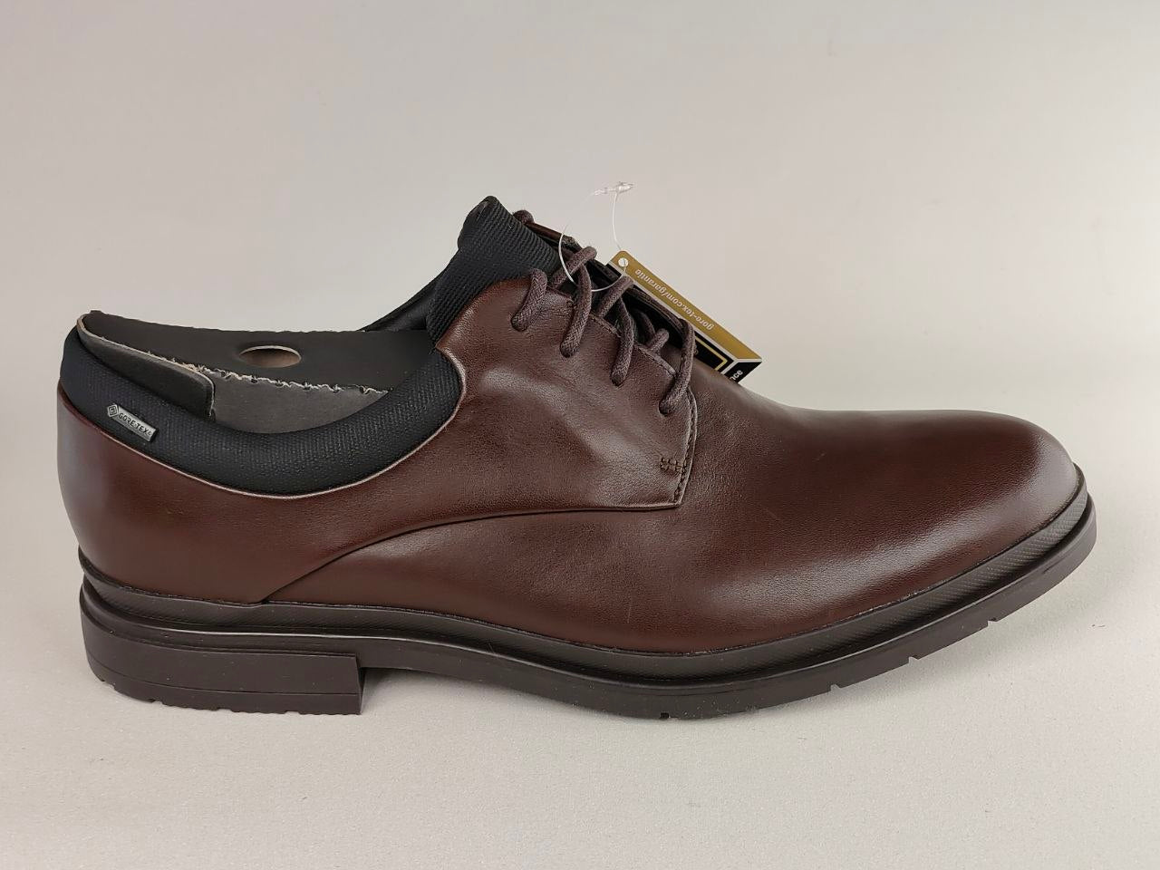 Brown leather shoe with black sole on a light gray background
