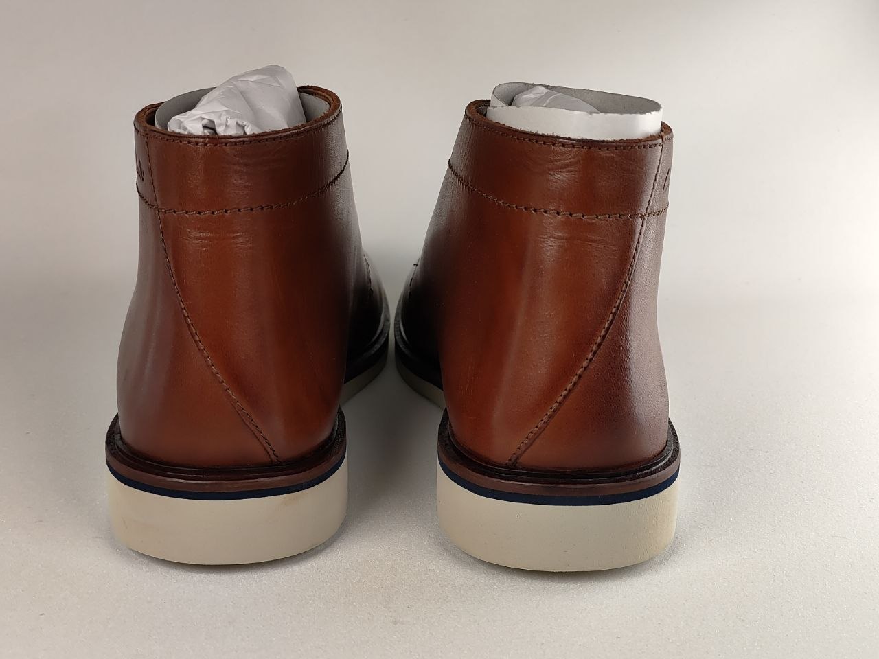 Pair of brown leather boots with white soles on a light gray background
