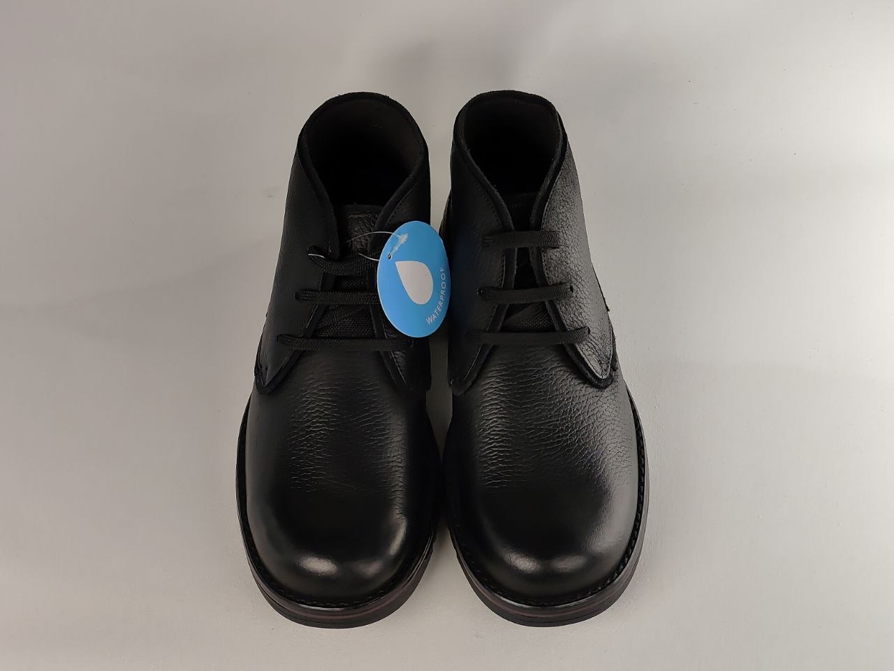 Pair of black leather shoes with a blue tag on a light gray background