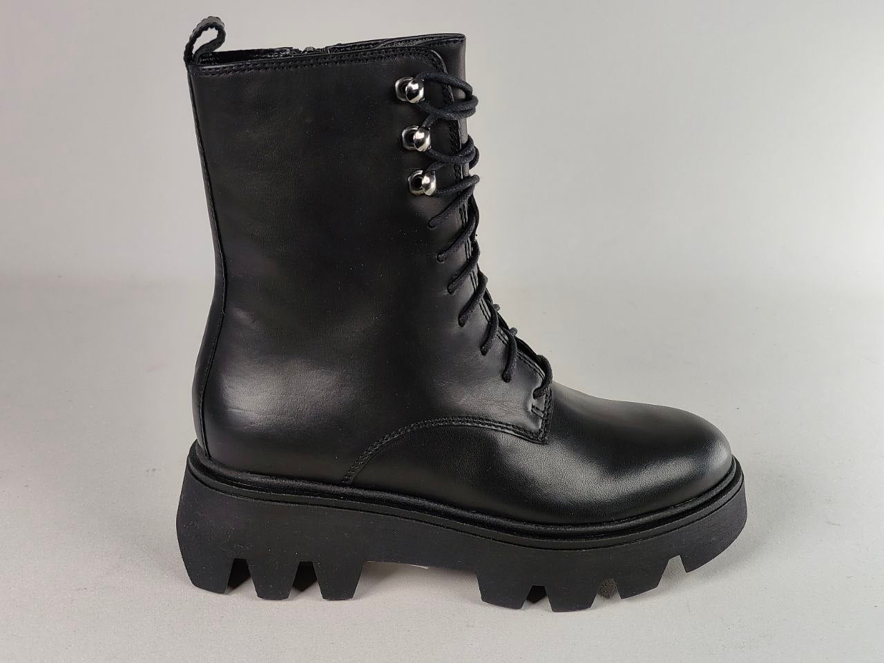 A single black leather lace-up ankle boot with a chunky lug sole and silver metal eyelets, photographed against a neutral light gray background.