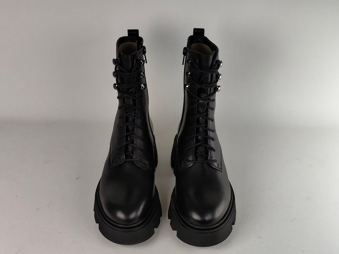 A pair of black leather lace-up ankle boots with chunky lug soles, photographed from the front against a light gray studio background.