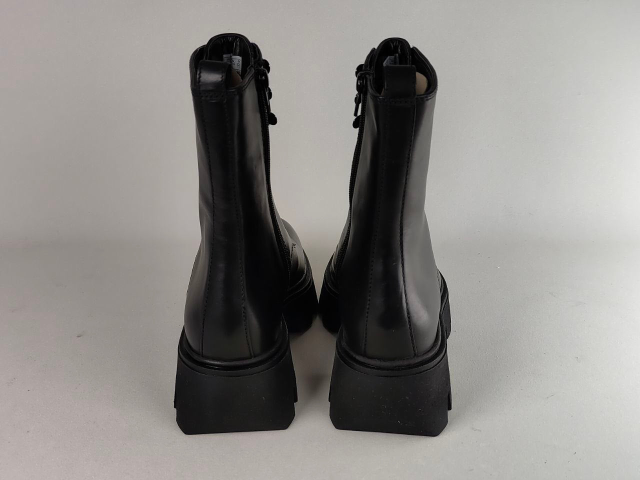 A pair of black leather ankle boots with chunky platform block heels, shown from the back against a neutral light gray background.