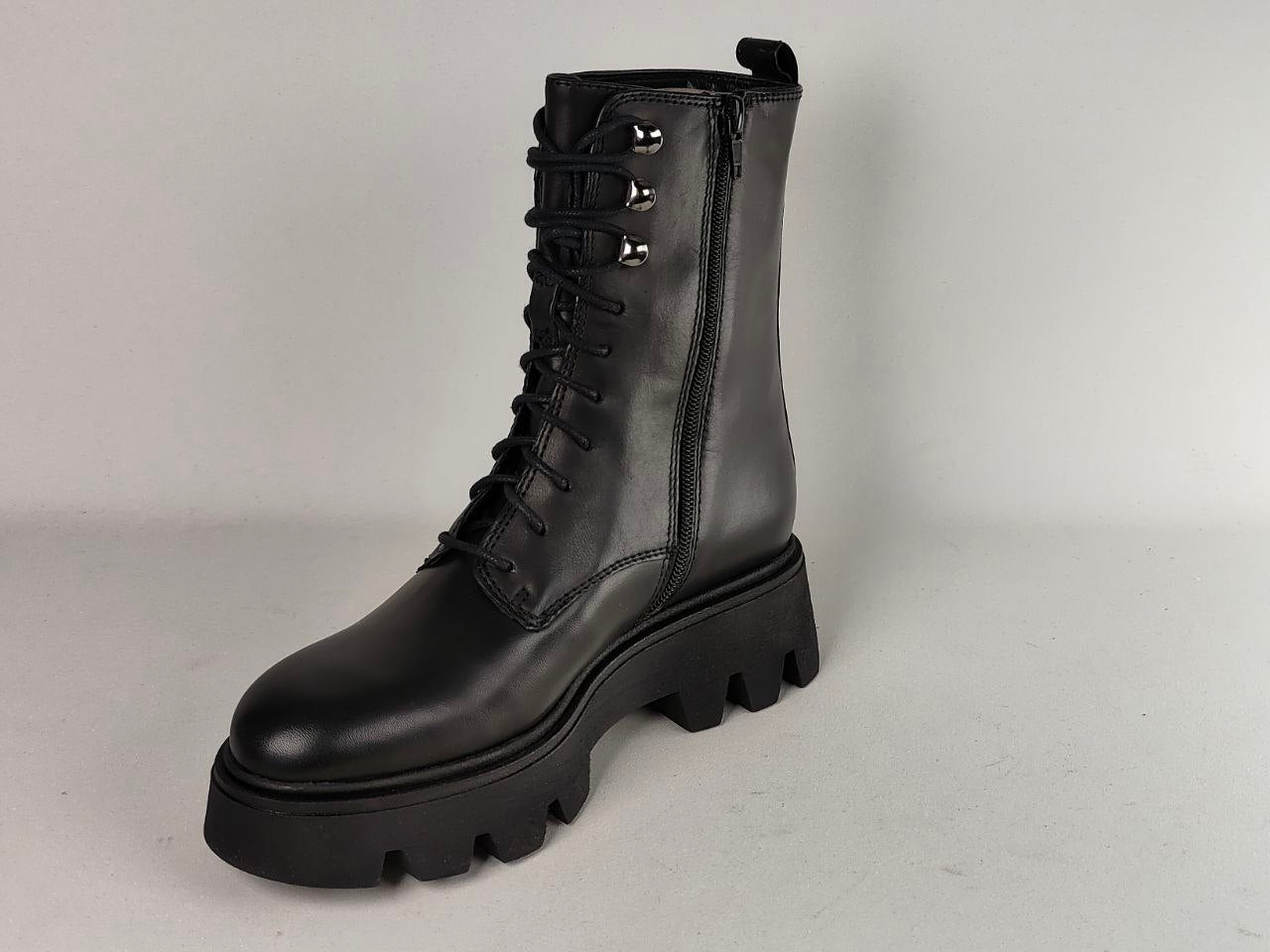 A black leather lace-up ankle boot with a thick lug sole, side zipper, and silver metal eyelets, photographed on a light gray studio background.