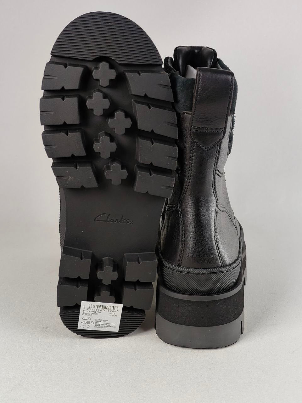Black leather ankle boots shown from the side and sole, featuring a chunky lug sole with a cross tread pattern and a platform heel, on a light gray background.