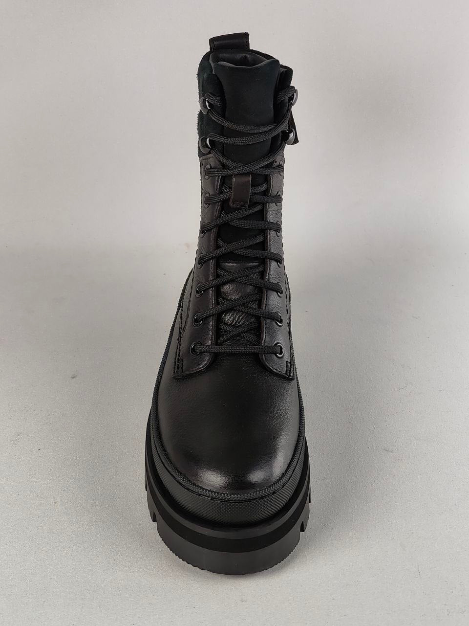 A single black leather lace-up ankle boot with a chunky platform sole, photographed from a front-facing angle against a neutral light gray background.