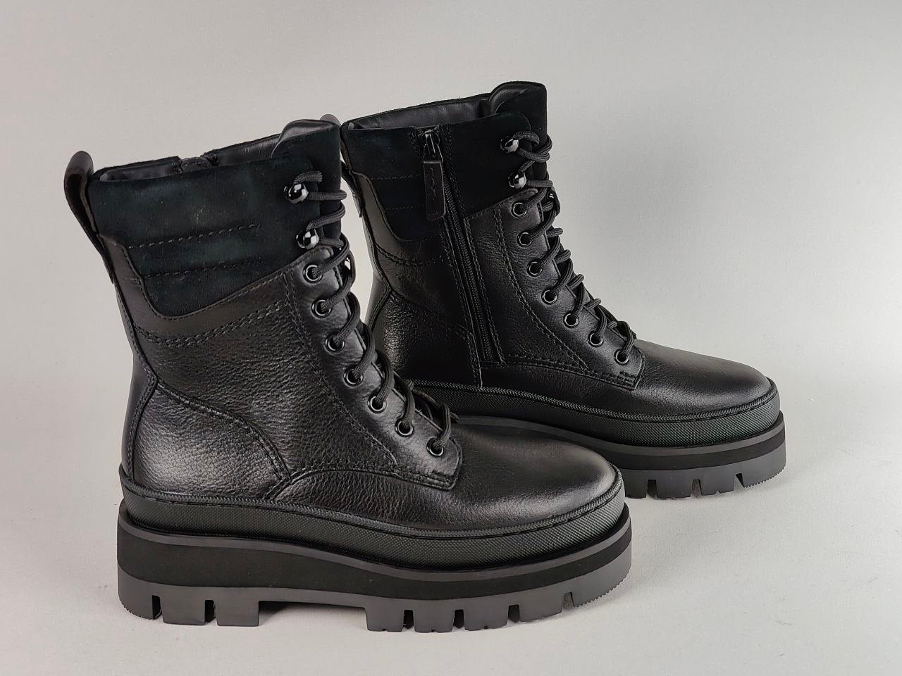 A pair of black leather lace-up ankle boots with side zippers, thick lug soles, and black laces, photographed on a neutral light gray background.