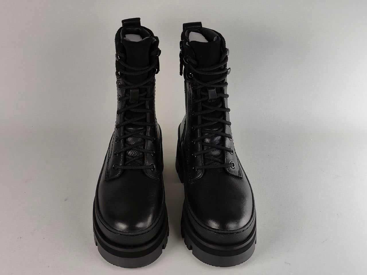 A pair of black leather lace-up combat boots with chunky platform soles, photographed from the front against a light gray background.