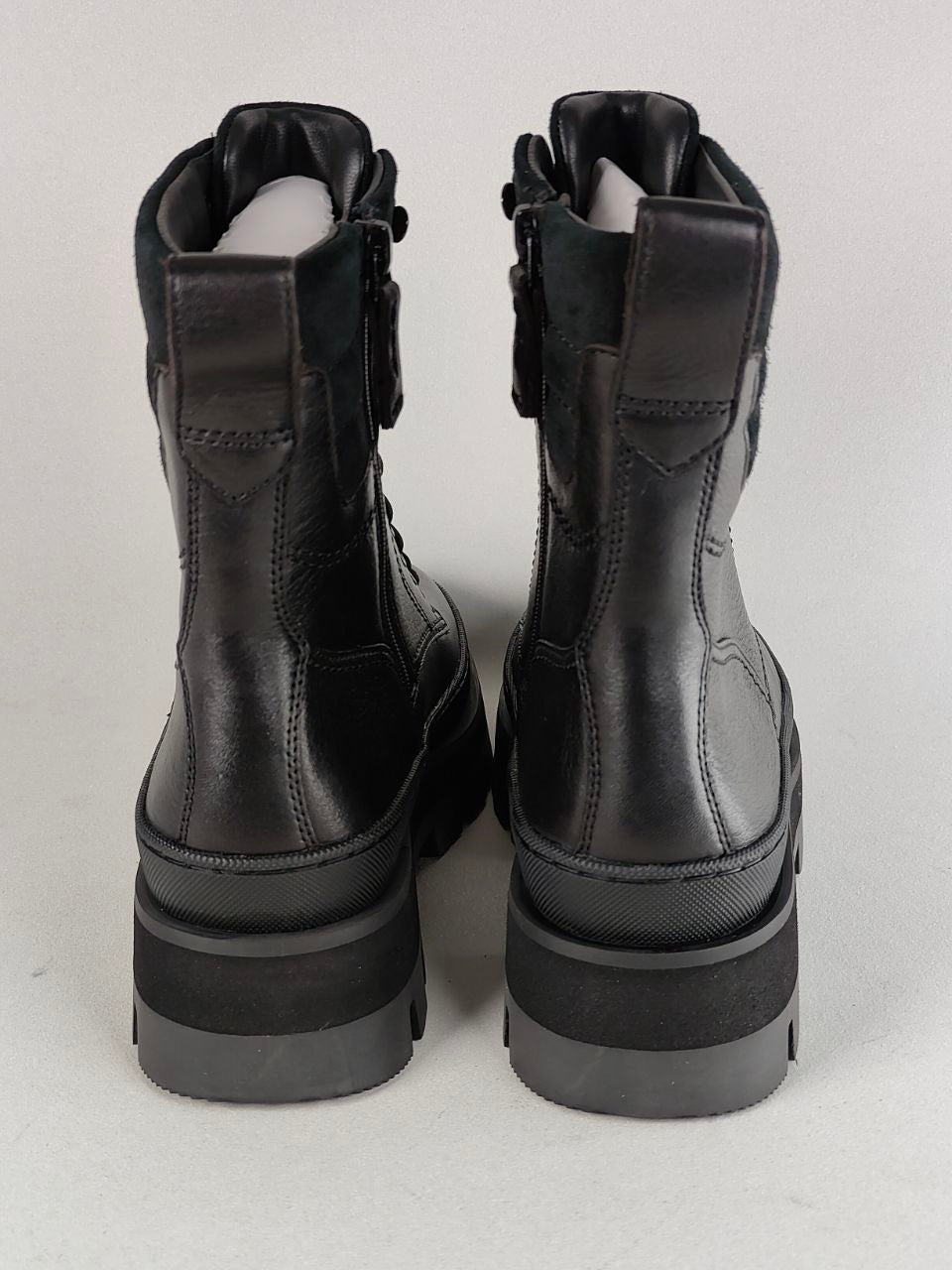 A pair of black leather ankle boots with chunky platform soles and side zippers, shown from the back on a light gray background.