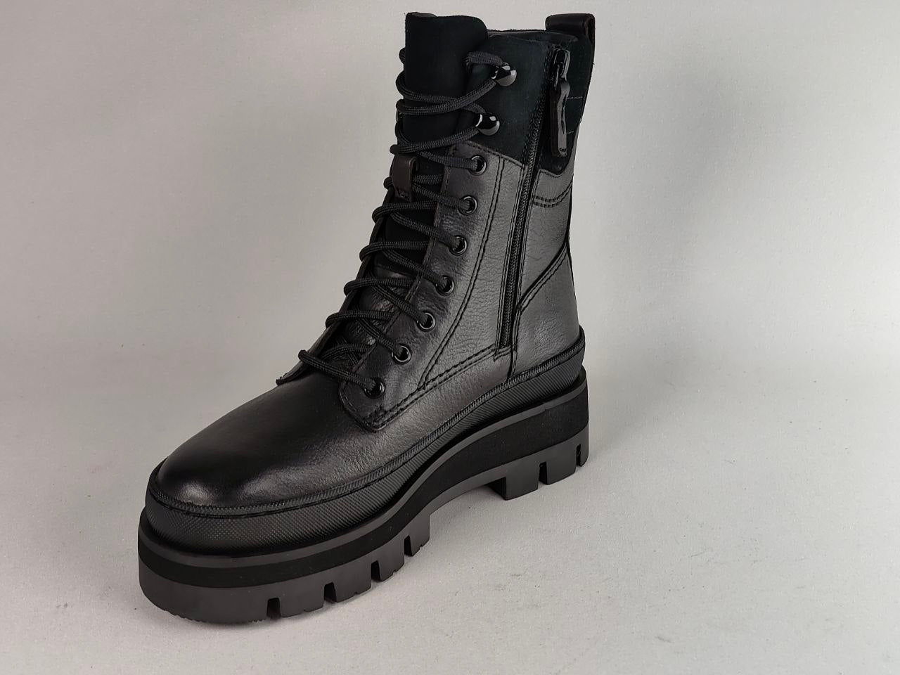 A black leather lace-up combat boot with a thick lug sole and side zipper, photographed on a neutral light gray background.