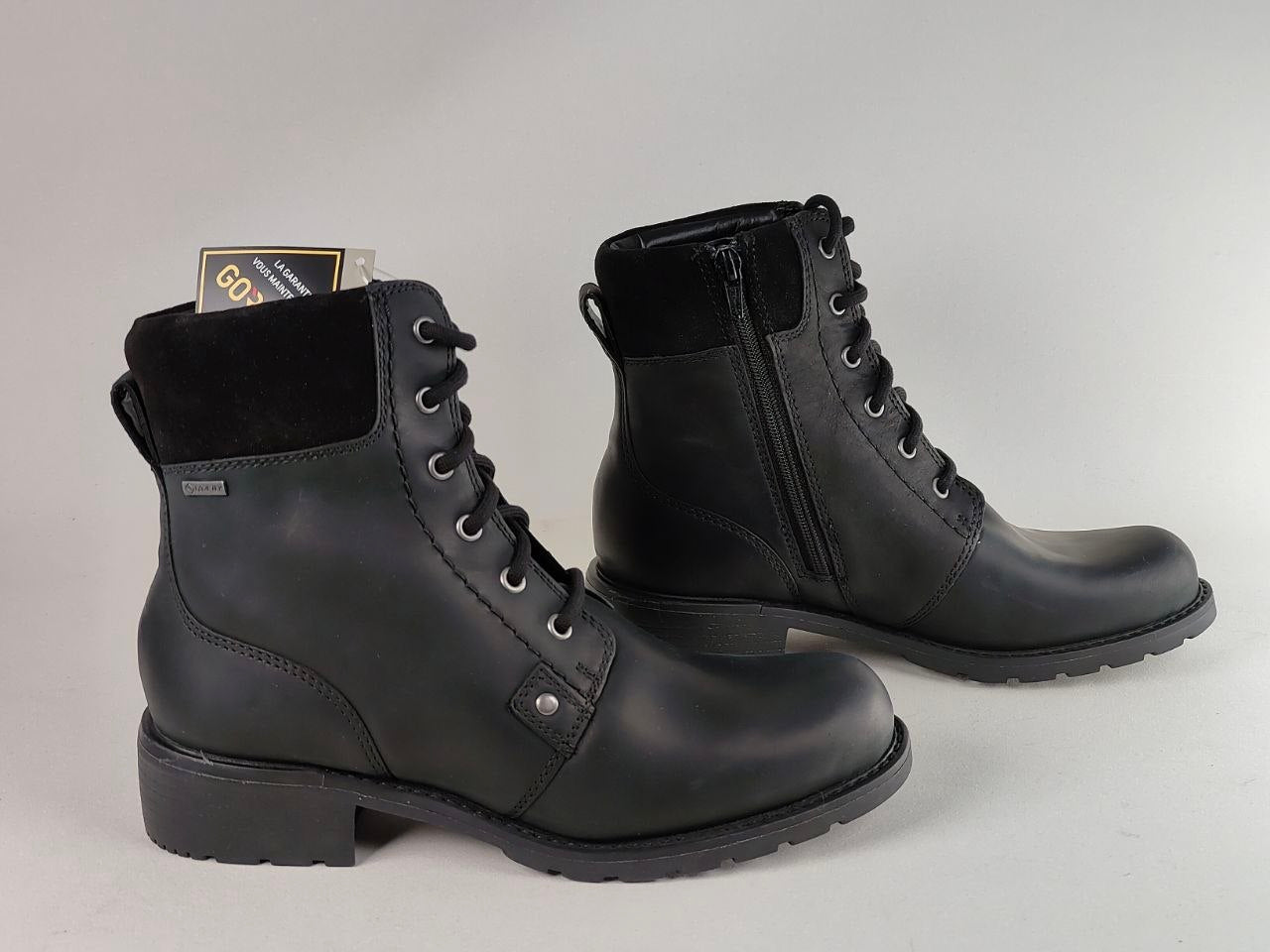A pair of black leather lace-up ankle boots with black fleece trim and side zippers, displayed on a light gray background.