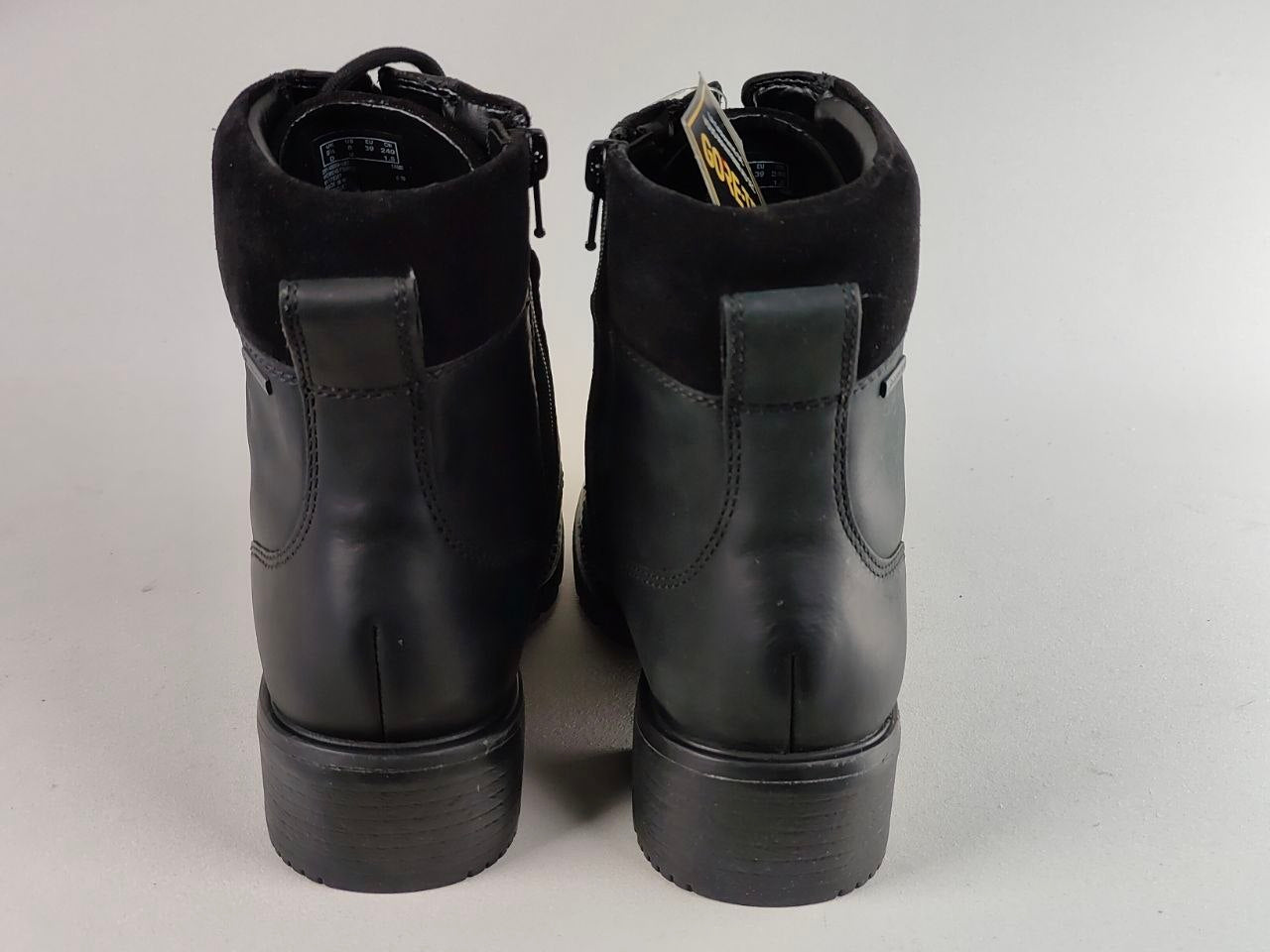 A pair of black leather ankle boots with a suede-like collar, shown from the back on a light gray background.