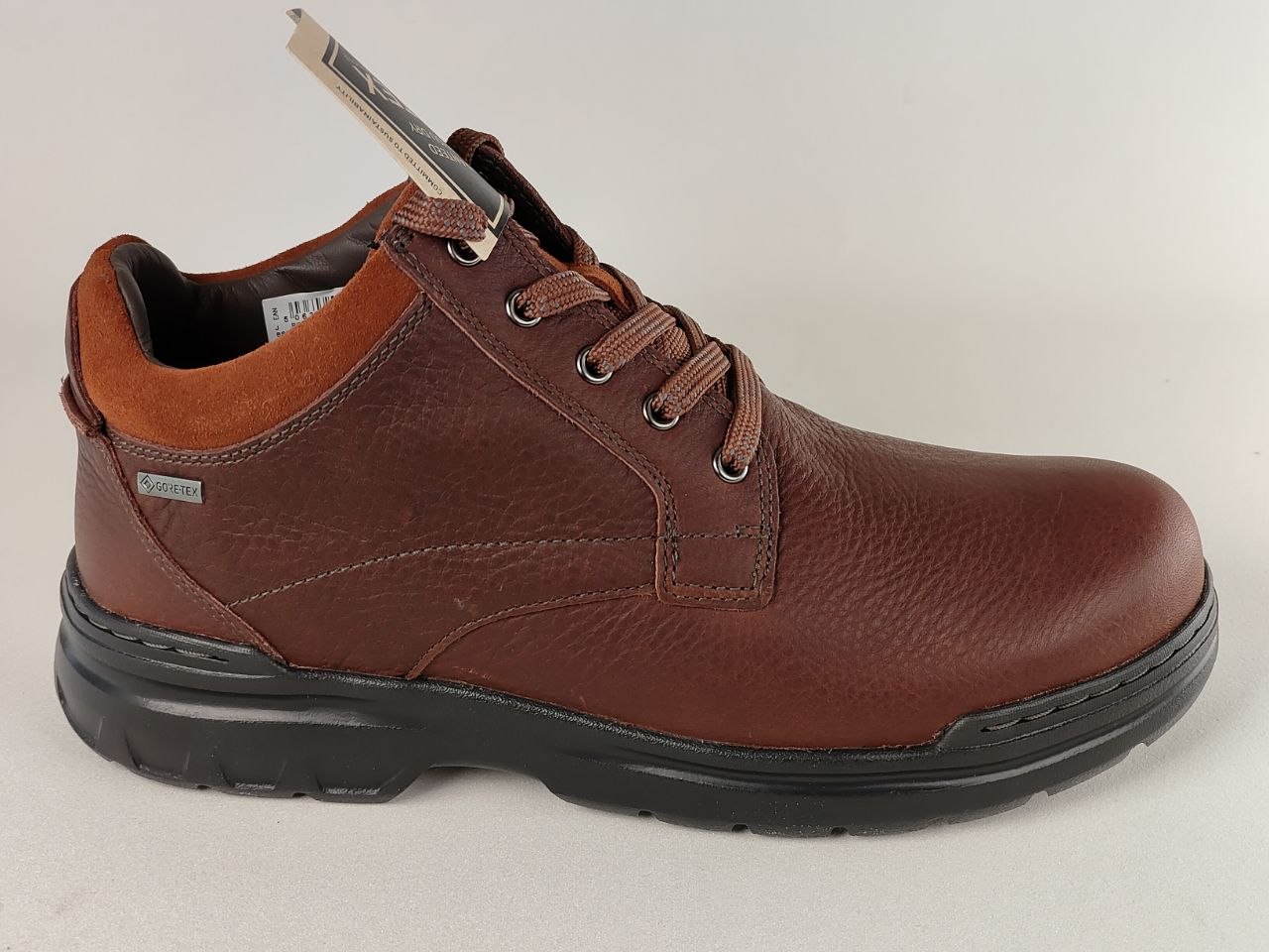 Brown leather shoe with black sole on a light gray background