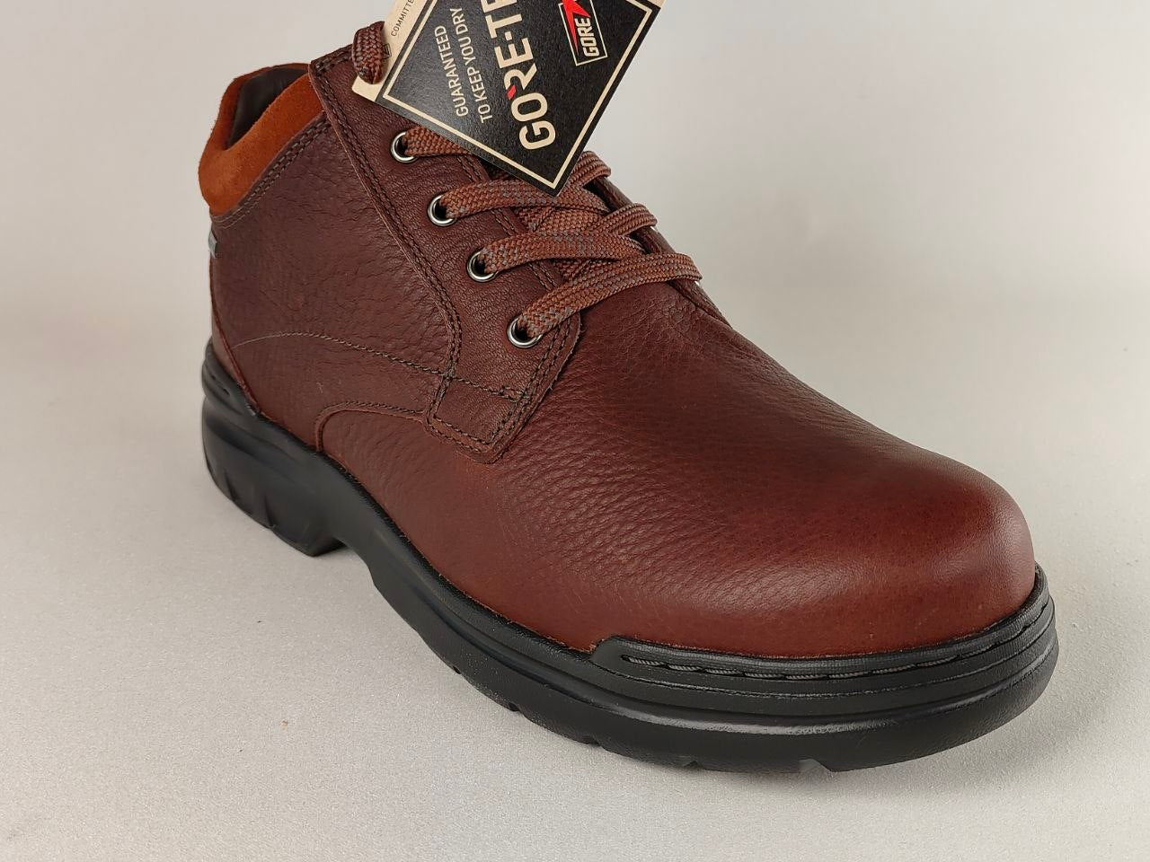 Brown leather shoe with a visible brand tag on a light gray background