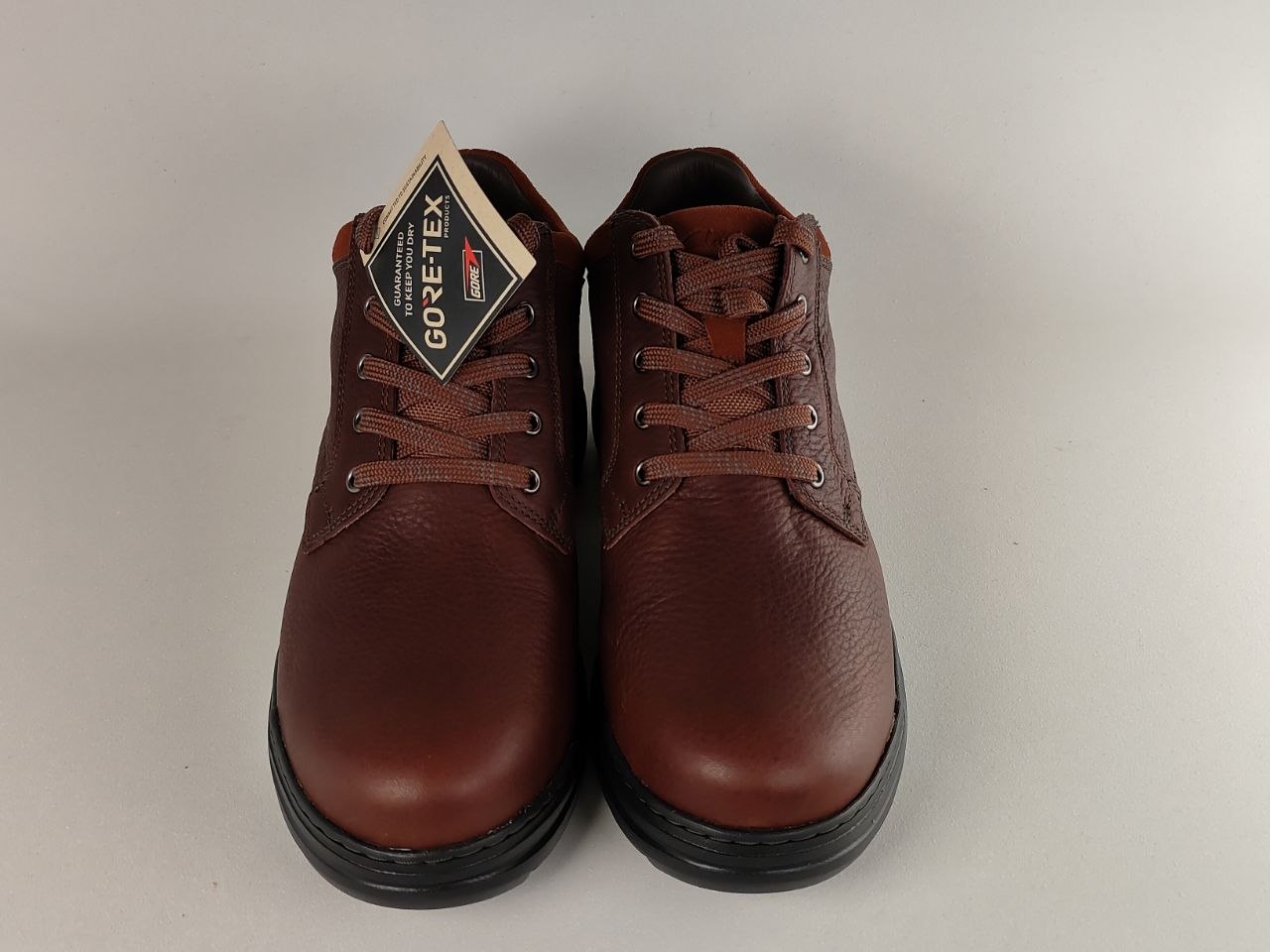 Pair of brown leather shoes with a Goretex tag on a light gray background