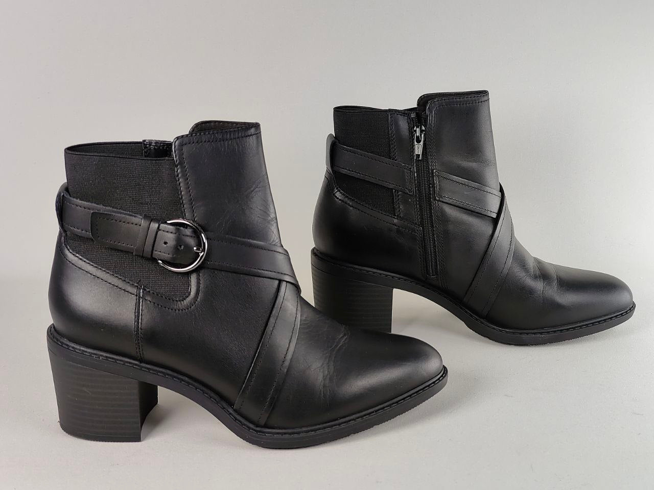 A pair of black leather ankle boots with side buckles and block heels, photographed on a neutral light gray background.
