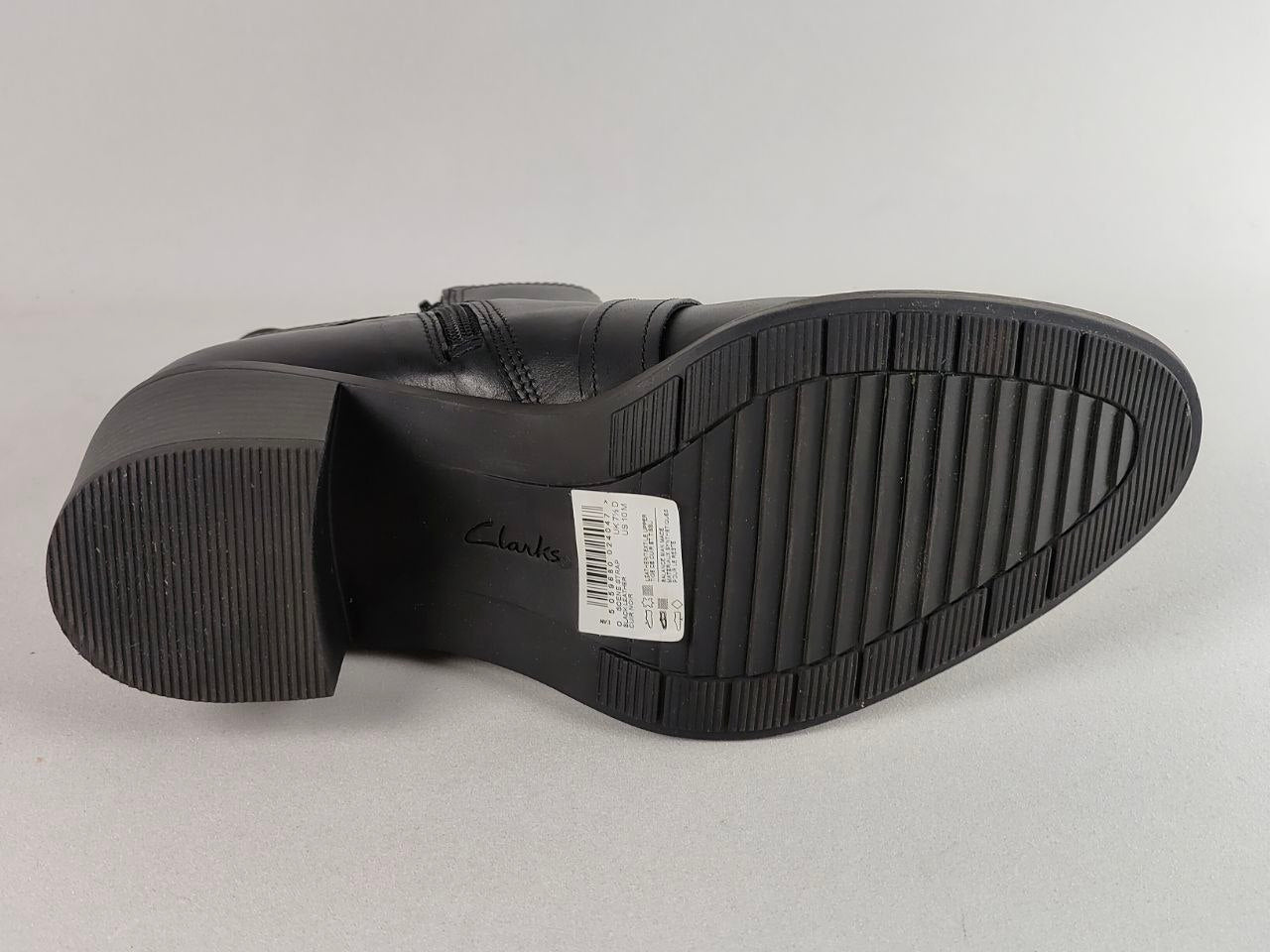 Black leather boot sole showing the tread pattern, heel, and a white size label, photographed on a light gray background.