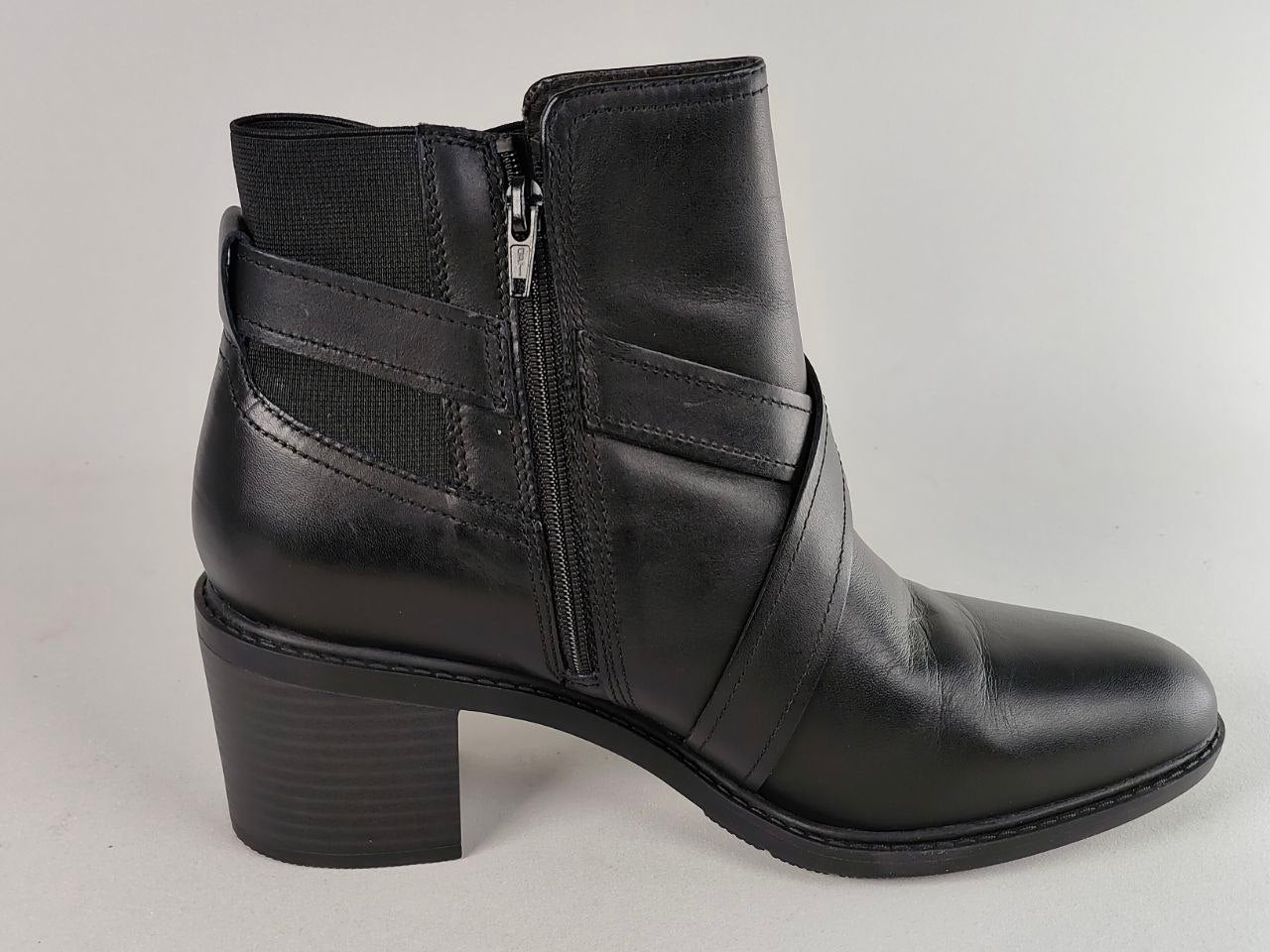 A black leather ankle boot with a side zipper, a thick block heel, and decorative straps on the side, shown against a light gray background.