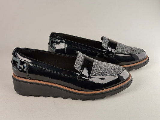 Black patent leather loafers with glittery accents on a light gray background