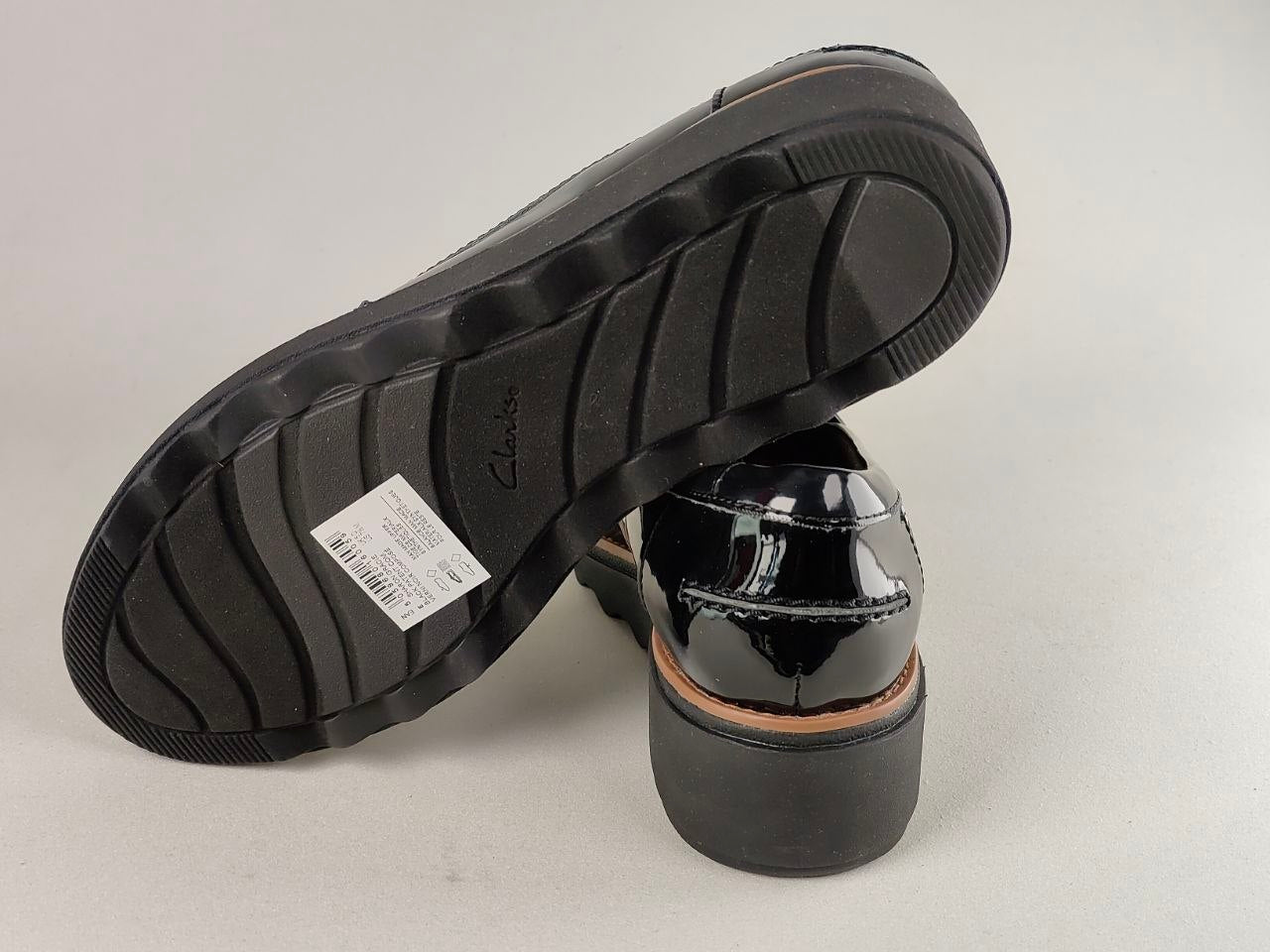Black patent leather shoe with a visible brand label on a light gray background