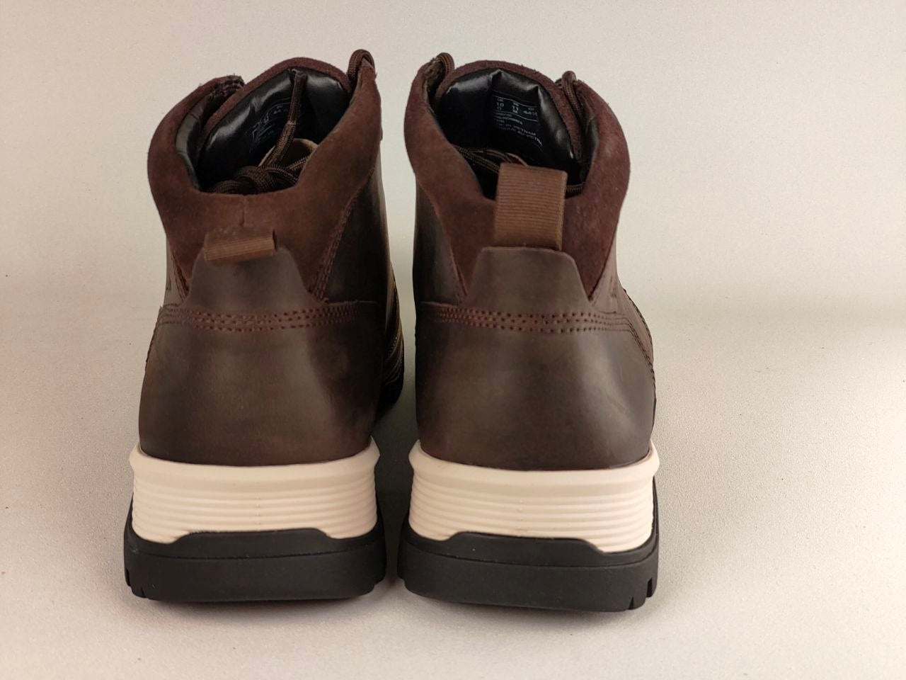 Pair of brown leather boots with white soles on a beige background