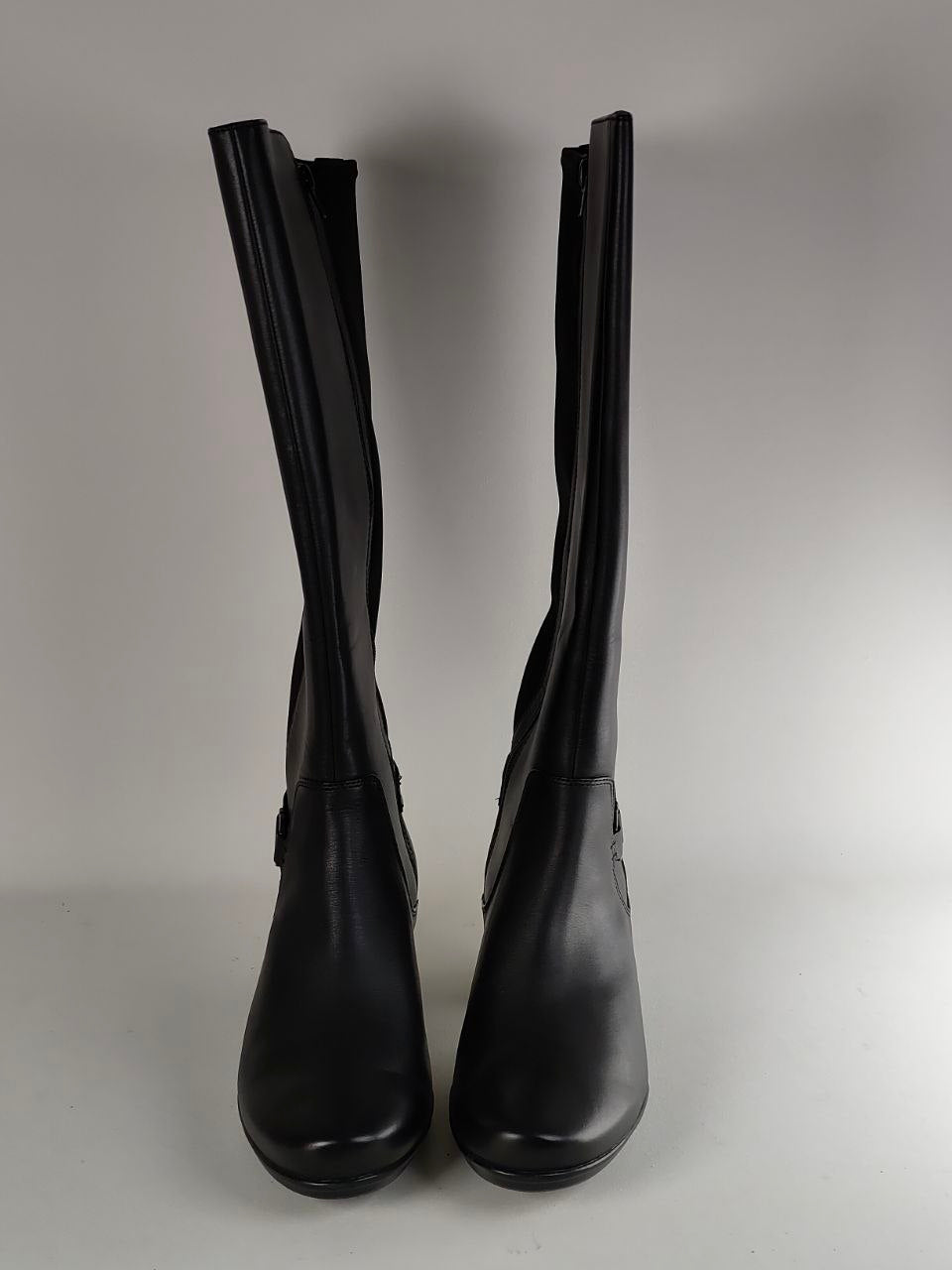 A pair of black leather knee-high boots with side zippers and low block heels, photographed against a neutral gray background.