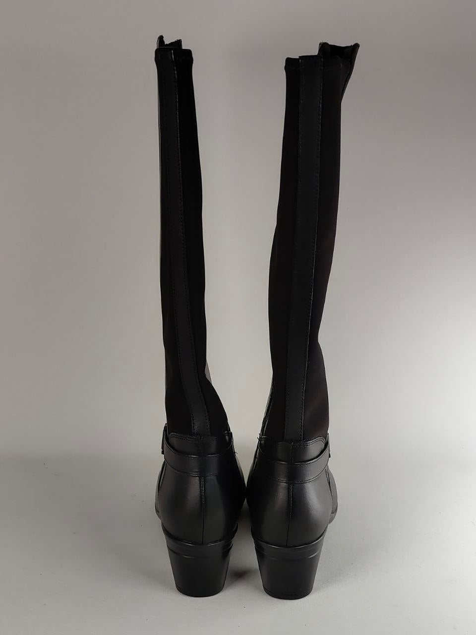 Black over-the-knee boots with a high block heel, shown from the back against a neutral gray background.