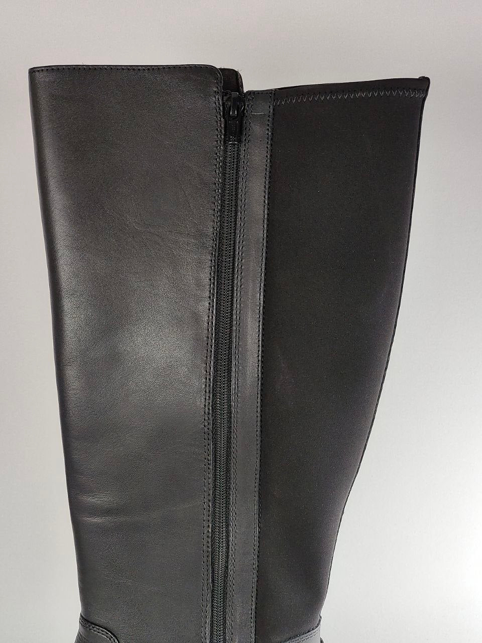 A close-up of a black leather knee-high boot featuring a central front zipper, set against a neutral light gray background.