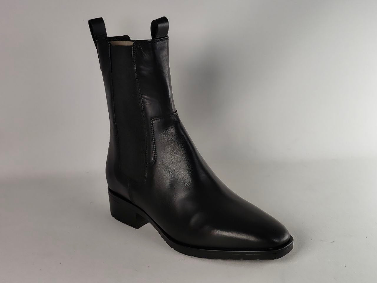 A single black leather Chelsea-style ankle boot with a low block heel and pull tabs at the top, photographed on a light gray studio background.