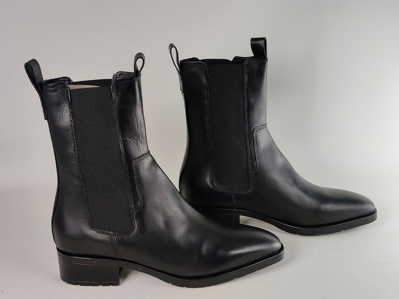 A pair of black leather Chelsea-style ankle boots with black elastic side panels, shown on a light gray studio background.