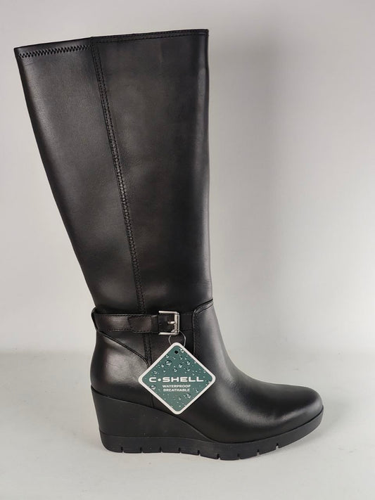 A black leather knee-high boot with a wedge heel, ankle strap, and buckle, featuring a hanging C-SHELL brand tag, photographed against a neutral gray background.